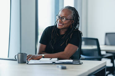 Experienced black business woman smiling and looking at her computer screen as she works on a task. Mature female professional using her expertise to achieve success in a business office. - JLPPF01885