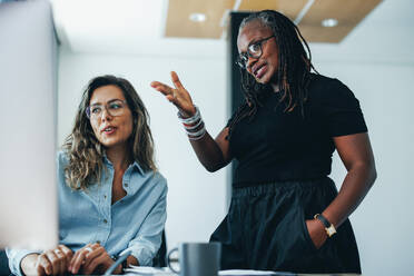 Ältere schwarze Geschäftsfrau, die ihr Fachwissen mit ihrer Kollegin teilt, während sie gemeinsam an einem Projekt am Computer arbeiten. Zwei weibliche Geschäftsleute, die als Team in einem Startup arbeiten. - JLPPF01888