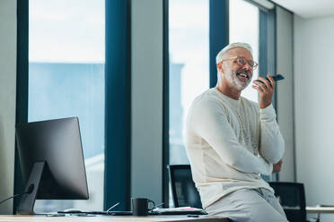 Successful business man with experience smiles as he speaks with his colleagues on the phone. Mature entrepreneur discussing his latest business ventures on a phone call. - JLPPF01892