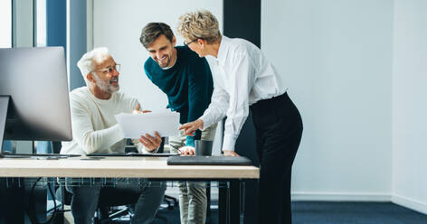 Three business people huddling and discussing a document in an office. Group of business professionals contributing their ideas and expertise as they collaborate on a project for their startup. - JLPPF01894