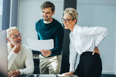 Geschäftsleute, die ein Dokument besprechen, während sie in einem professionellen Umfeld zusammenarbeiten. Gruppe von Geschäftsleuten, die in einem Büro ein Brainstorming durchführen und ihr Fachwissen austauschen. - JLPPF01895