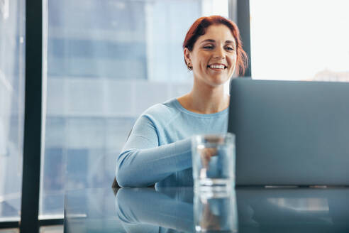 Eine glückliche junge Frau nimmt an einer Online-Geschäftsbesprechung teil und bringt ihre Erkenntnisse in das Gespräch ein. Eine Geschäftsfrau benutzt einen Laptop, um mit ihrem Team aus der Ferne zu kommunizieren. - JLPPF01906