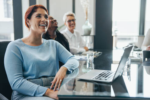 Eine weibliche Führungskraft lächelt, während sie aufmerksam einer Geschäftspräsentation im Sitzungssaal eines Büros zuhört. Eine glückliche junge Geschäftsfrau, die an einer Sitzung teilnimmt, um die Ziele ihres Teams zu unterstützen. - JLPPF01911