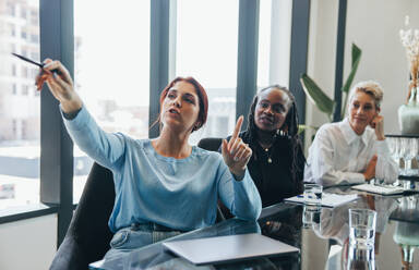 Junge Unternehmerin stellt ihrem Team während einer Geschäftsbesprechung ihre innovativen Ideen vor und regt zur Zusammenarbeit an. Geschäftsfrau leitet ihre Kollegen bei einem Projekt an. - JLPPF01914