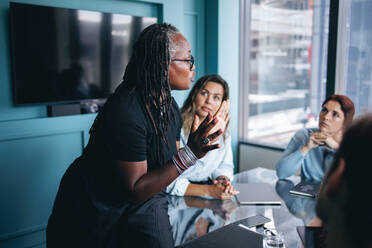 Reife schwarze Geschäftsfrau, die ihre Strategie mit ihrem Team, einer Gruppe verschiedener Fachleute, bespricht. Erfahrene Unternehmerin, die ein gemeinsames Geschäftstreffen in einem Büro leitet. - JLPPF01973