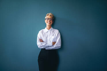 Portrait of a confident and professional business woman standing in her workplace at a financial company. Successful career woman smiling at the camera with crossed arms. - JLPPF01981