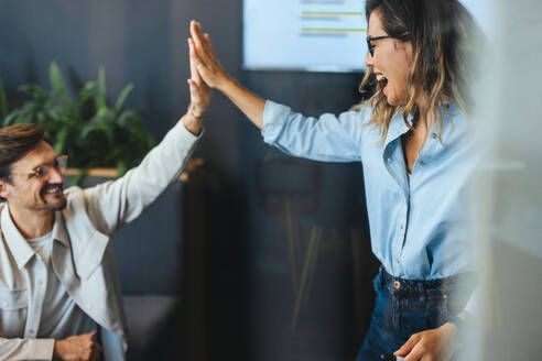 Happy business colleagues high five each other, celebrating their teamwork and success on a major business project. Two business people working together for the growth of their company. - JLPPF01994