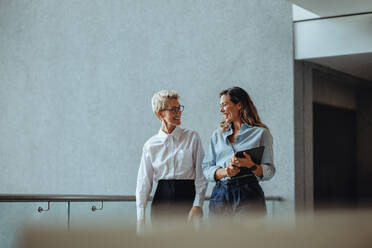 Zwei Geschäftsfrauen unterhalten sich lächelnd in einem professionellen Büro. Eine reife Frau lässt sich von ihrer Verwaltungsassistentin über die Leistung des Unternehmens informieren. - JLPPF02037