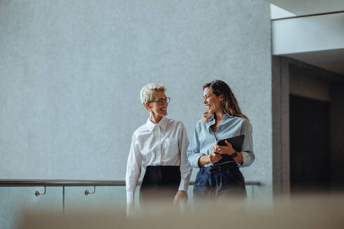 Zwei Geschäftsfrauen unterhalten sich lächelnd in einem professionellen Büro. Eine reife Frau lässt sich von ihrer Verwaltungsassistentin über die Leistung des Unternehmens informieren. - JLPPF02037