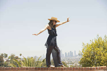 Junge Frau balanciert auf einer Backsteinmauer - FOLF12129