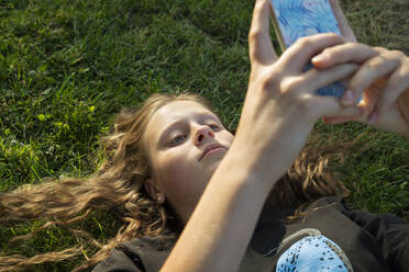 Mädchen benutzt Smartphone im Gras liegend - FOLF12155