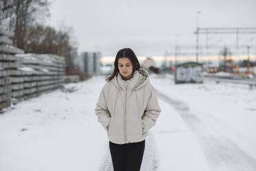 Young woman in jacket walking on road in snow - FOLF12177