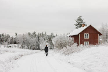 Frau geht an Hütte im Schnee vorbei - FOLF12180