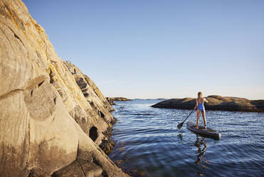 Mädchen Paddleboarding auf dem Meer durch Felsen - FOLF12237