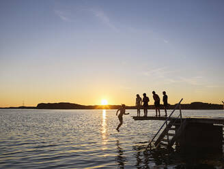 Kinder springen bei Sonnenuntergang vom Steg ins Meer - FOLF12248