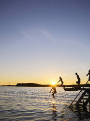 Children diving from jetty into sea at sunset - FOLF12250