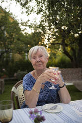 Ältere Frau hält Weinglas am Tisch im Garten - FOLF12256