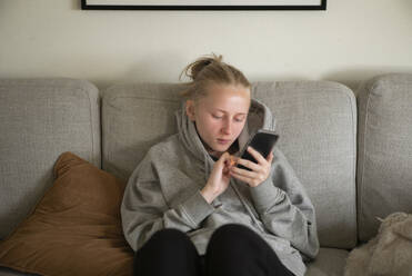 Junge Frau benutzt ihr Smartphone auf dem Sofa - FOLF12260