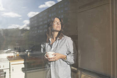 Woman holding coffee cup by window - FOLF12333