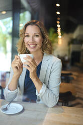 Smiling businesswoman holding cup at cafe - PNEF02841