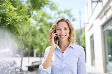 Lächelnde Frau mit blondem Haar, die mit einem Smartphone telefoniert - PNEF02848