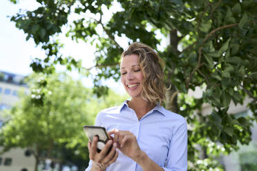 Lächelnde Frau, die eine Textnachricht über ihr Smartphone verschickt - PNEF02855