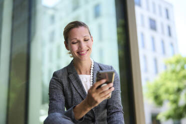 Smiling businesswoman surfing net through smart phone - PNEF02865