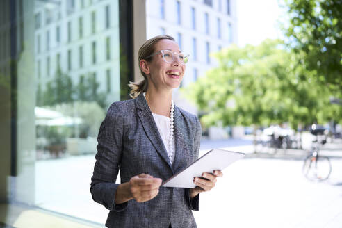 Happy businesswoman holding tablet PC near building - PNEF02877