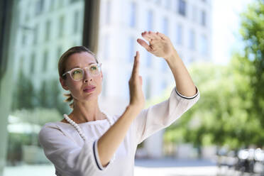 Businesswoman wearing eyeglasses and gesturing near building - PNEF02885