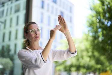 Geschäftsfrau gestikuliert mit den Händen in der Nähe eines Gebäudes - PNEF02886