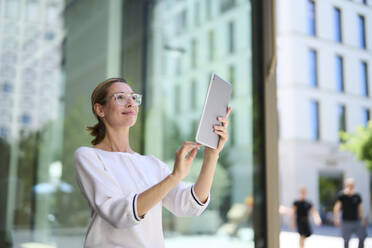 Smiling businesswoman using tablet PC near building - PNEF02890