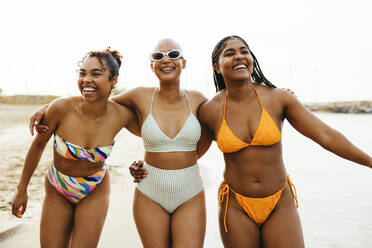 Carefree friends in swimwear with arms around at beach - EBSF03350