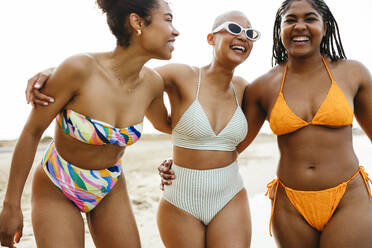 Playful friends in swimwear with arms around at beach - EBSF03351