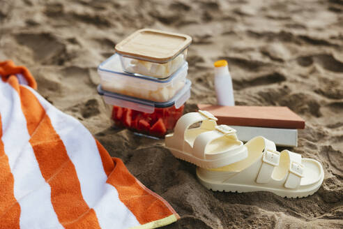 Sandalen und Obstbehälter mit Handtuch im Sand am Strand - EBSF03372