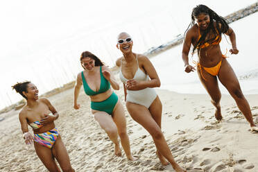 Fröhliche Freundinnen in Bikinis, die am Strand im Sand laufen - EBSF03401