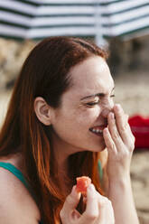 Glückliche Frau mit geschlossenen Augen, die ihre Nase am Strand berührt - EBSF03404