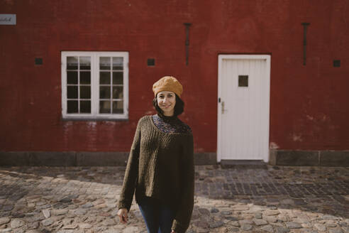 Frau steht auf einer Kopfsteinpflasterstraße vor einem roten Gebäude - GMLF01472