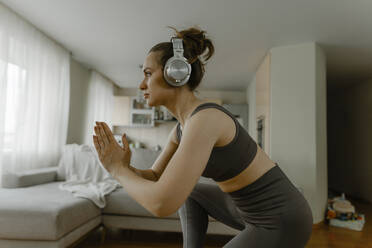 Determined woman with headphones practicing yoga in living room - IEF00352