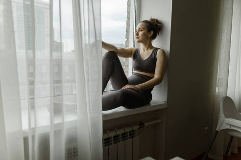 Nachdenkliche Frau, die sich zu Hause auf der Fensterbank ausruht - IEF00357