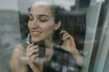 Lächelnde Frau schaut aus einem Glasfenster - IEF00366