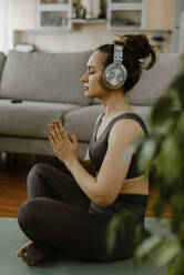 Frau mit Kopfhörern beim Meditieren im Wohnzimmer - IEF00368