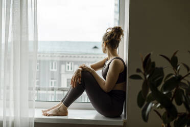 Nachdenkliche Frau schaut aus dem Fenster und sitzt zu Hause - IEF00374