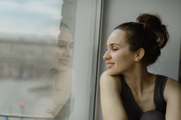 Smiling woman looking out of window at home - IEF00382