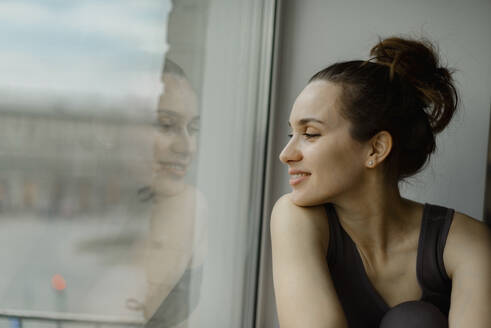 Lächelnde Frau schaut zu Hause aus dem Fenster - IEF00382