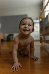 Smiling baby girl crawling in bedroom - IEF00393