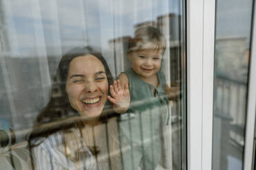 Glückliche Mutter und Tochter spielen in der Nähe des Fensters durch Glas gesehen - IEF00403