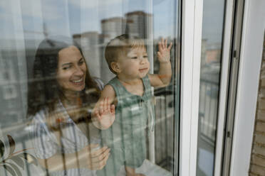 Verspielte Mutter mit kleinem Mädchen schaut aus einem Glasfenster - IEF00404