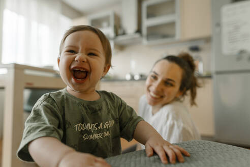 Cheerful baby girl laughing with mother in kitchen - IEF00408