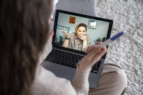 Frau zeigt einem Freund per Videoanruf über Laptop ein Schwangerschaftstestkit - VPIF08021