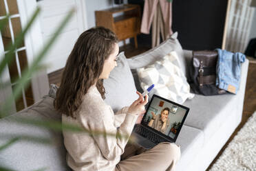 Happy woman showing pregnancy testing kit to friend on video call over laptop - VPIF08023